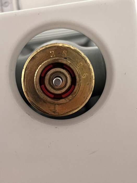 Rund radiatorventil med röda detaljer och siffrorna 2, 5, 0, 5, monterad i ett vitt element. Ventilen är omgiven av en cirkulär ram.