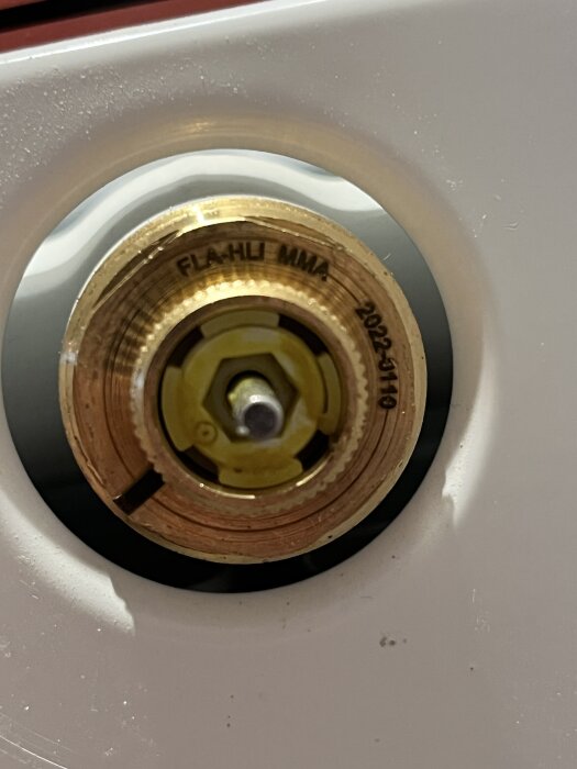 Närbild av en termostatventil på ett element, märkt "FLA-HLI MMA 2022-11-10", med en gul och röd detalj synlig i centrum.