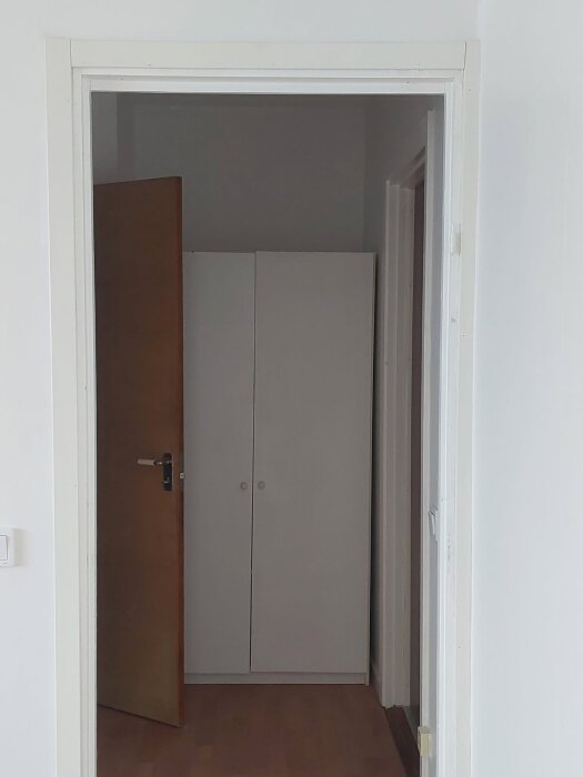 Öppen dörr som leder till ett rum med en vit garderob och trägolv, del av renoveringsprojekt.