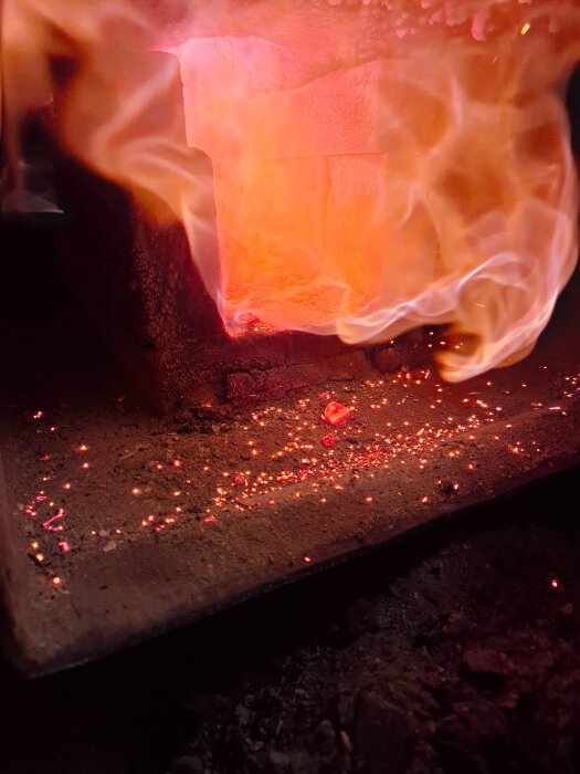 Rödorange glöd och flammor i en ugn eller eldstad, med gnistor och värme som strålar ut från den heta ytan.