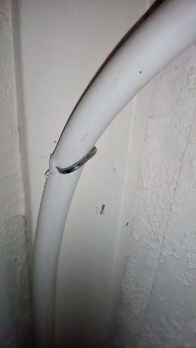 En vit kabel i ett hörn med en liten skada och en kabelklammer som håller den på plats. Bakgrunden är en ljus vägg med textur.