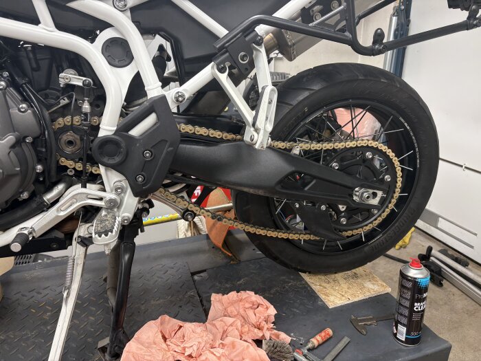 Motorcykel med nytt kedje- och drevsystem på en upplyft plats, omgiven av verktyg och rengöringsspray.