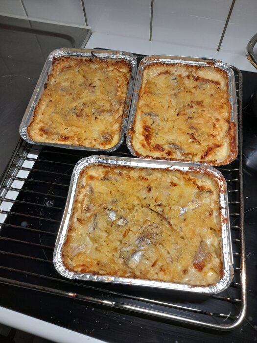 Tre gratängformar med Jansson frestelse nygratinerade på köksbänk.