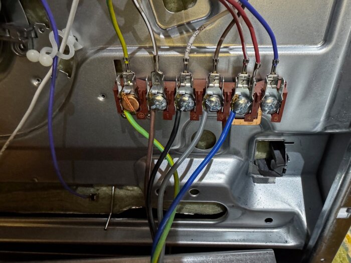 Närbild av elektriska anslutningar med färgkodade kablar inuti en apparat, fästa vid märken numrerade 1 till 5.