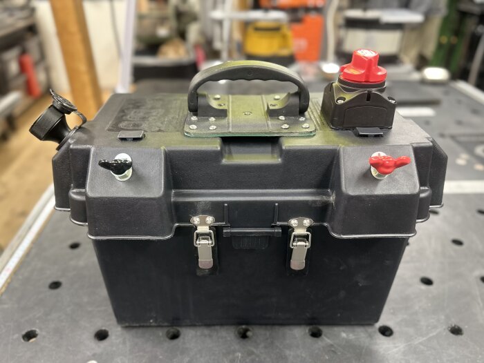 Ett svart batterifodral med handtag, anslutningsplintar och huvudbrytare, anpassat för ett 170Ah litiumbatteri, på en arbetsyta.
