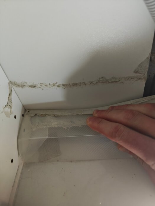 Hand håller i plastskydd i skåphörn, visar problem med passform och tejp för fastsättning.