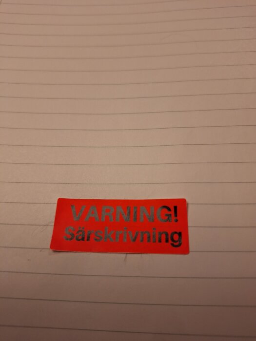 Röd klisterlapp på linjerat papper med texten "VARNING! Särskrivning".