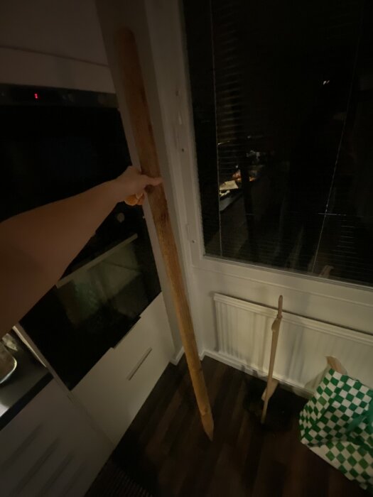 En person håller en lång trästolpe inomhus.