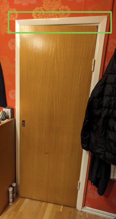 Trädörr som är monterad för högt i karmen, överdelen markerad med en grön ruta, vilket orsakar problem med att stänga.