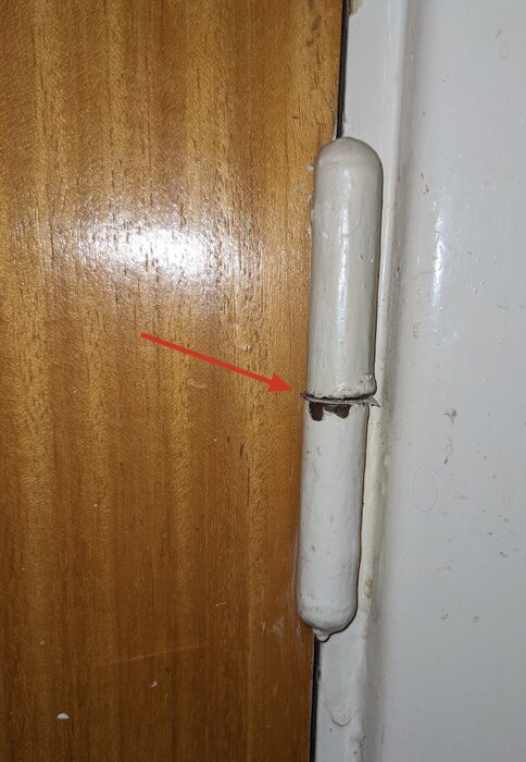 Övre gångjärnet på en dörr som inte går att stänga, med rött streck som visar luft mellan gångjärnet och karmen.