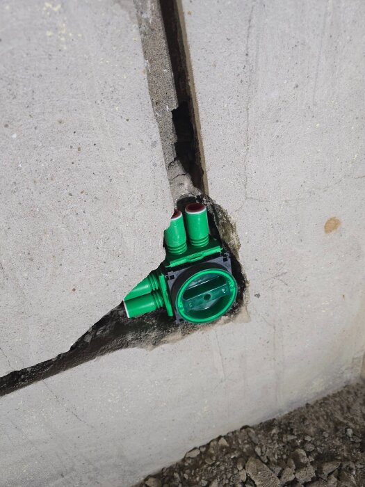 En vägg av betong med ett eluttag och gröna flexrör delvis installerade i en uppsågad öppning.