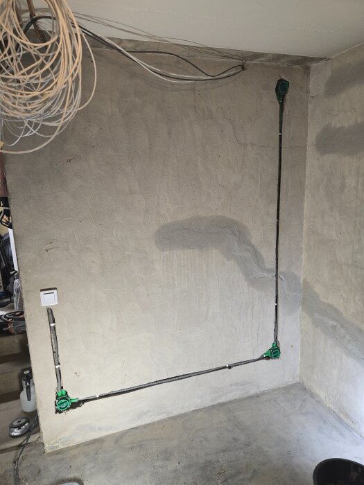Bärande vägg med elinstallation, synliga kablar och gröna eldosor nära golv och tak. Vägg förberedd för fler uttag i renoveringsprojekt.
