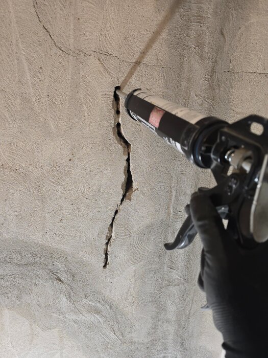 Person fyller spricka i vägg med lagningsbruk och fogpistol, del av renoveringsprojekt för att förbättra elinstallation och förbereda dörr.