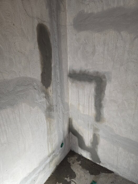 Betongvägg med nyspacklade ytor och en installerad eluttagdosa i ett hörn. Väggarna visar tecken på fukt och pågående renovering.