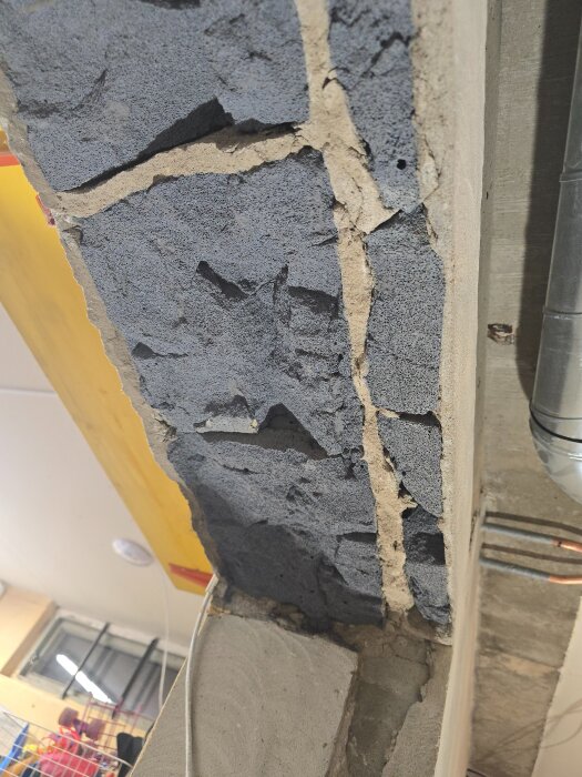 Sprucken vägg i blåbetong med synlig armering och sprickor runt ett dörrhål i en renoveringsprocess.