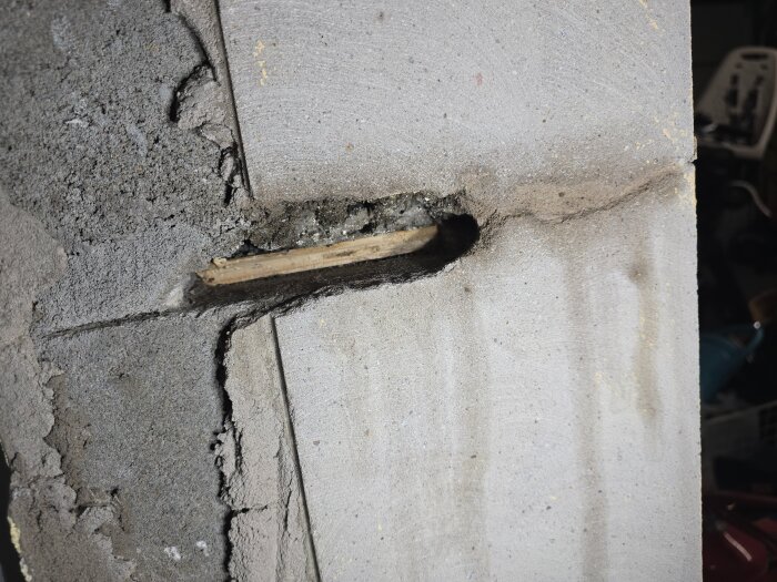 Spricka i en betongvägg med en träbit synlig i öppningen, upptäckt under renovering av ett dörrhål i ett garage.