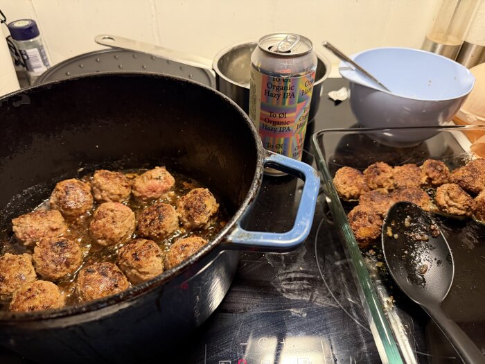 Köttbullar steks i en stor gryta på spisen, med en blå skål och en ölburk i bakgrunden.