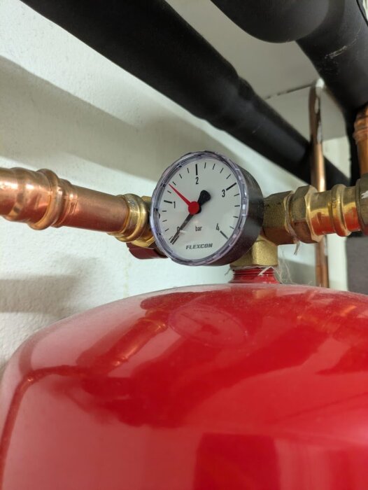 Manometer på 1,3 bar monterad på röd expansionskärl, kopparrör och svarta isolerade rör i bakgrunden.