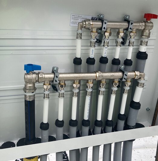 Vattenfördelarskåp med anslutna PEM-rör, blå och röd ventil synliga. Utförd installation med press-PEX enligt monteringsanvisning.
