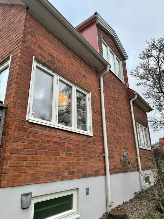 Tegelliksnande fasad på äldre hus med vita fönster och stuprännor, där fasaden diskuterats att ersättas för bättre isolering och estetik.