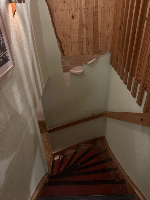 Trappa med slitna väggar, delvis med panel och sönderriven tapet, för renovering av ett Anebyhus från 1971, sedd uppifrån.
