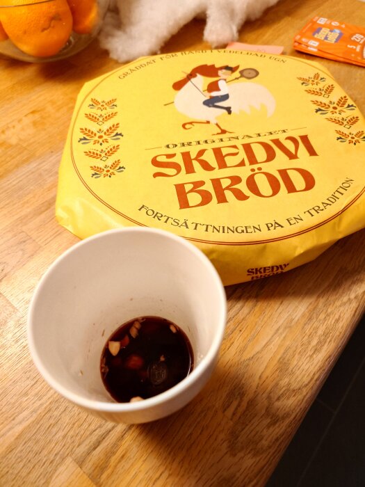 En skål med glögg och nötter bredvid ett paket Skedvi bröd på en träbordsyta.