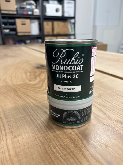 En burk Rubio Monocoat Oil Plus 2C i färgen Super White står på ett träbord, används för ytbehandling av träytor.