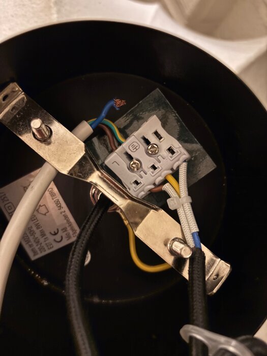 Inre delen av en lampa med sladdar, där en trasig plastdel hindrar en blå sladd från att fästas ordentligt.