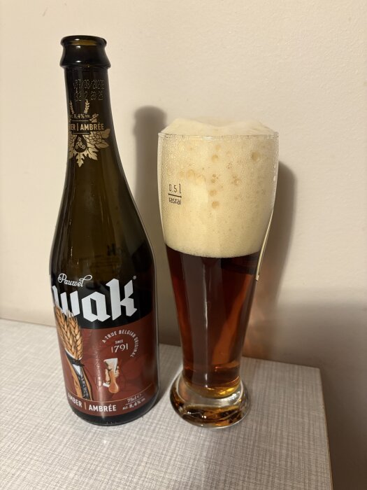 Belgiskt öl av märket Kwak, flaska bredvid glas fyllt med bärnstensfärgad dryck och skummigt skum.