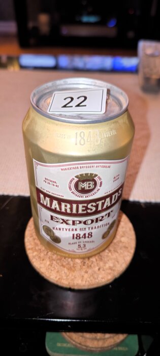 En Mariestads Export ölburk placerad på ett korkunderlägg med en nummerlapp märkt "22" på toppen.