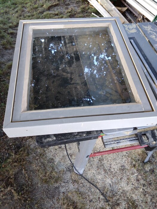 Gammalt fönster på ett arbetsbord utomhus. Fönstret har använts i ett hemmabyggt växthus.
