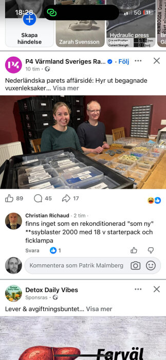 Två personer sitter vid ett bord med sorteringslådor fyllda av olika föremål och etiketter, omgivna av svarta lådor och en hylla i bakgrunden.