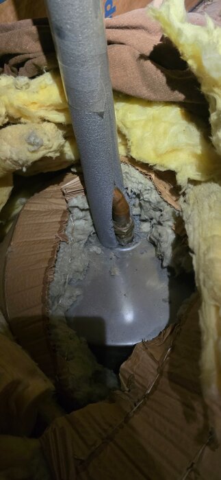 Isolerat rör med grå hylsa, omgiven av gul isolering och kartongmaterial, troligen i ett pågående bygg- eller renoveringsprojekt.