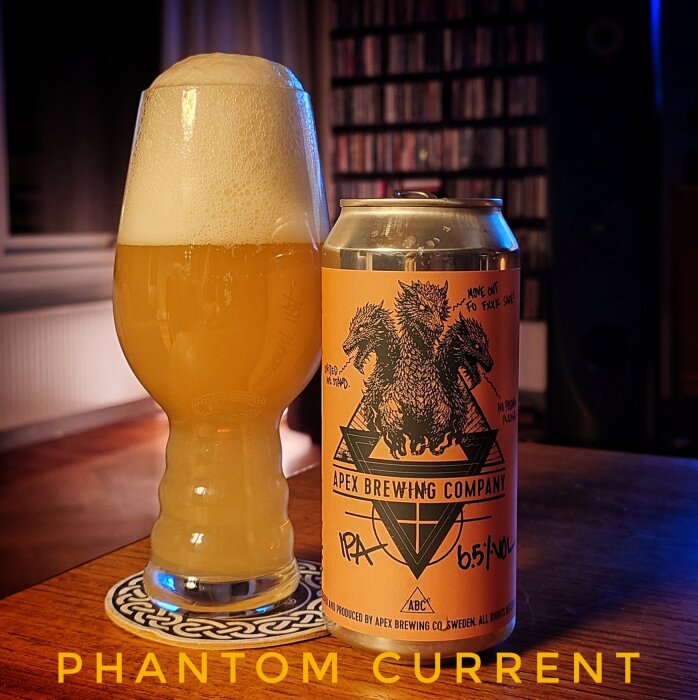Ölglas med skummande IPA bredvid en burk från Apex Brewing Company på ett bord.