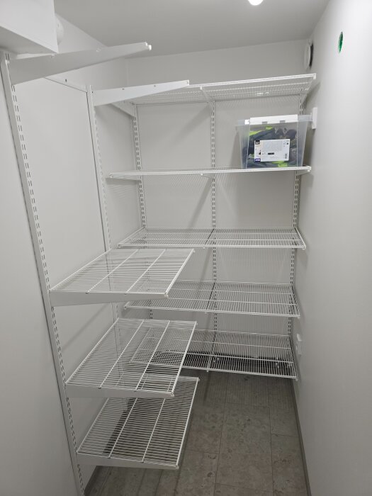 Vit hyllsystem i klädkammaren med flera vita trådhyllor, en plastlåda placerad på en av hyllorna, i en oinredd eller nyrenoverad miljö.