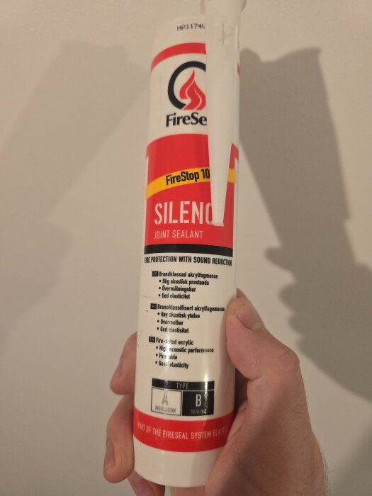 Förpackning av ljuddämpande och brandskyddande akrylfogmassa märkt "FireSeal Silence" hålls av en hand.