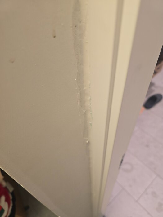 Vägg och dörrkarm i ett rum, med ljuddämpande fogmassa applicerad längs kanterna för att minska ljudläckage.