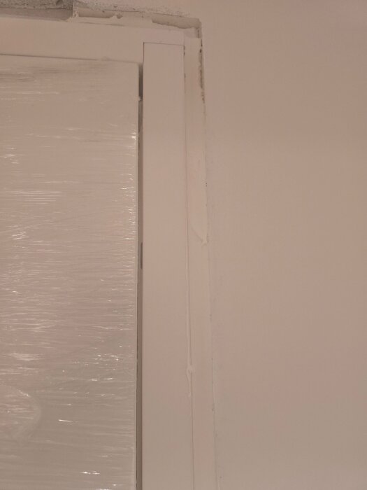 Närbild av dörrkarmens övre högerhörn med vitt drev och sprickor i väggen uppifrån, del av pågående renoveringsprojekt.