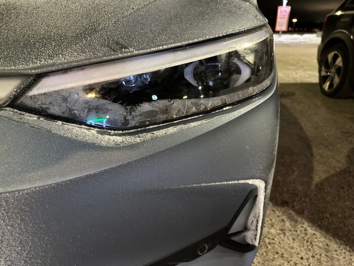 Närbild på en bilstrålkastare täckt av frost, taget på en vinterväg.