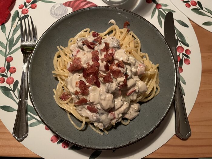 Tallrik med spaghetti toppad med krämig kycklingpastasås och baconcrunch, serverad på julbordstablett med bestick.