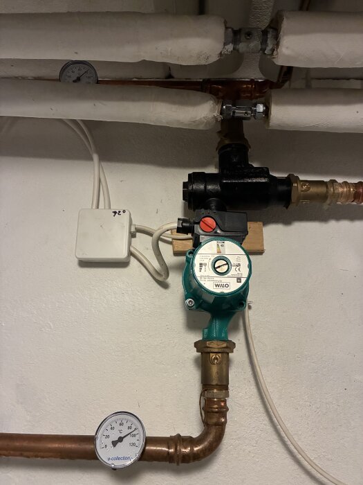 Cirkulationspump med termometer och rörkopplingar i ett värmesystem.