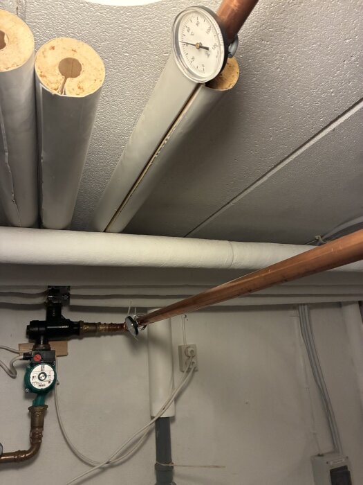 Värmesystem med kopparrör, värmeisolerade rör och en termometer som visar temperaturen, avstängd vedpanna samt cirkulationspump.