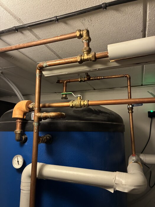 Vattenrör och kopparledningar anslutna till en blå ackumulatortank i en panncentral, med en tryckmätare synlig på tanken.