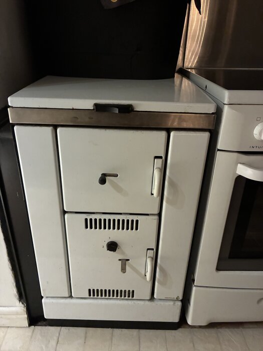 Vit Wamsler vedpanna bredvid en spis i ett kök, del av ett system för uppvärmning av ackumulatortank.