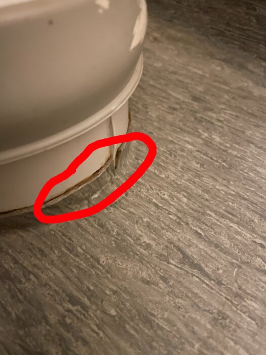 Läckage vid toalettens avlopp på golvmattan, markerat med röd cirkel.