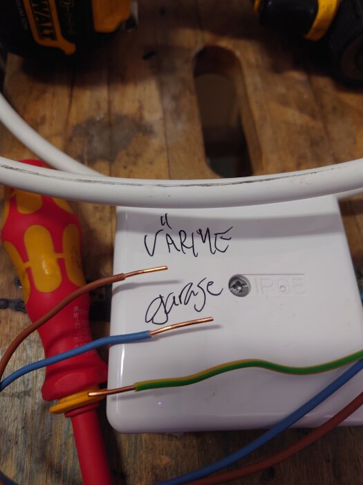 Olika elledningar och en skruvmejsel på en vit kopplingsdosa märkt "Värme Garage", med avskalade kablar synliga.