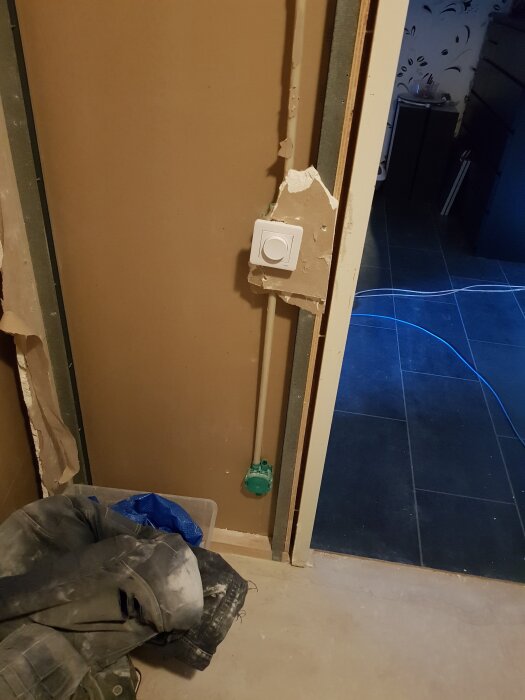 Pågående renovering av innervägg med synlig kabeldragning samt en dimmer installerad; byggdamm på golvet och kläder ligger i närheten.