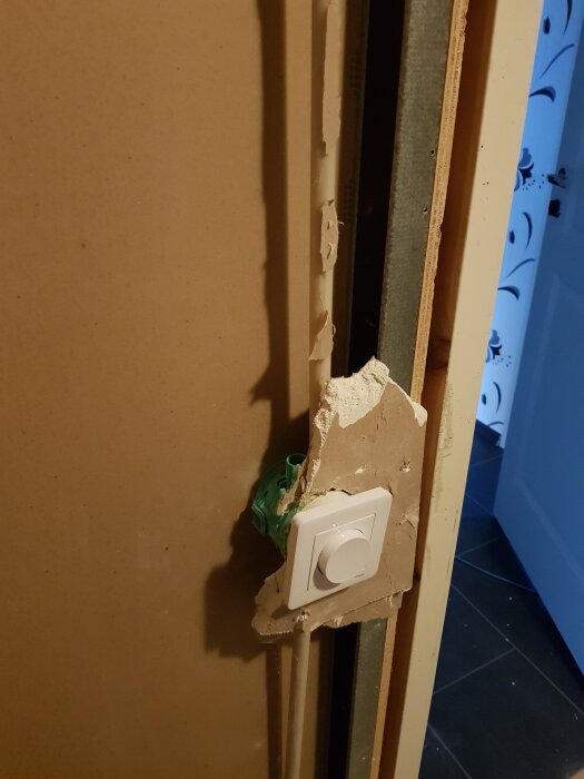 Trasig gipsskiva vid en dörrkarm med en dimmer installerad, visar en okonventionell renoveringssituation.