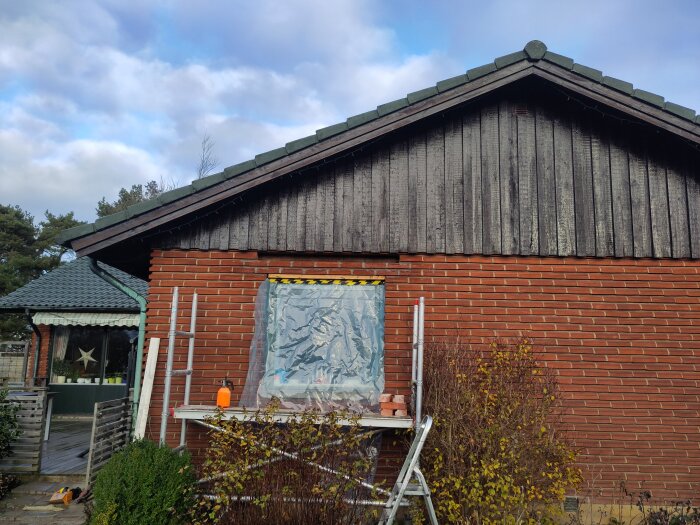 Tegelvägg med plasttäckta fönster, byggställning och stege framför. Förberett för murning på ett hus.