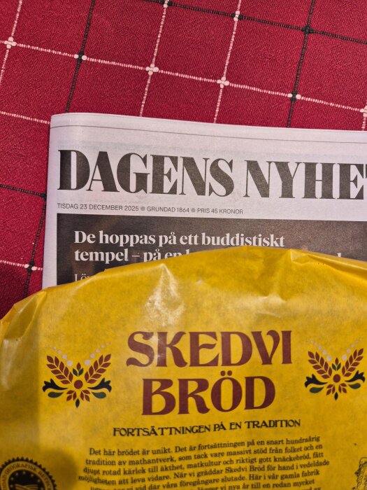 Förpackning av Skedvi bröd på en tidning med rubriken Dagens Nyheter, liggandes på en röd- och vitrutig duk.
